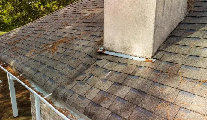 Worn asphalt shingles and flashing at a chimney on a roof