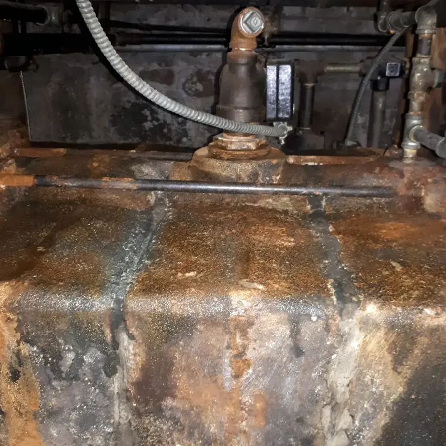 Rusted, leaking base of an old water heater tank